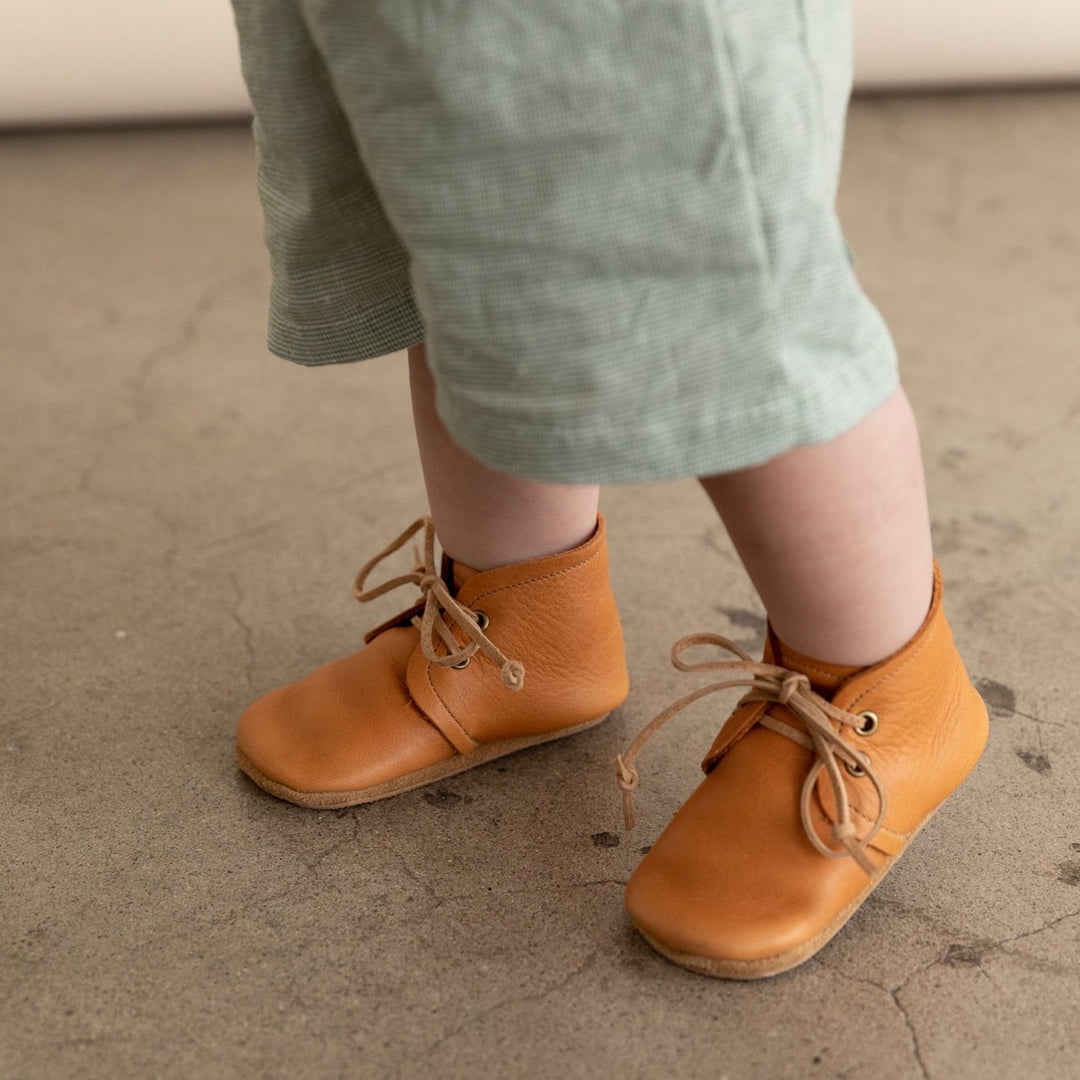 Ginger leather baby boots on walking feet. Soft soles on cement floor.