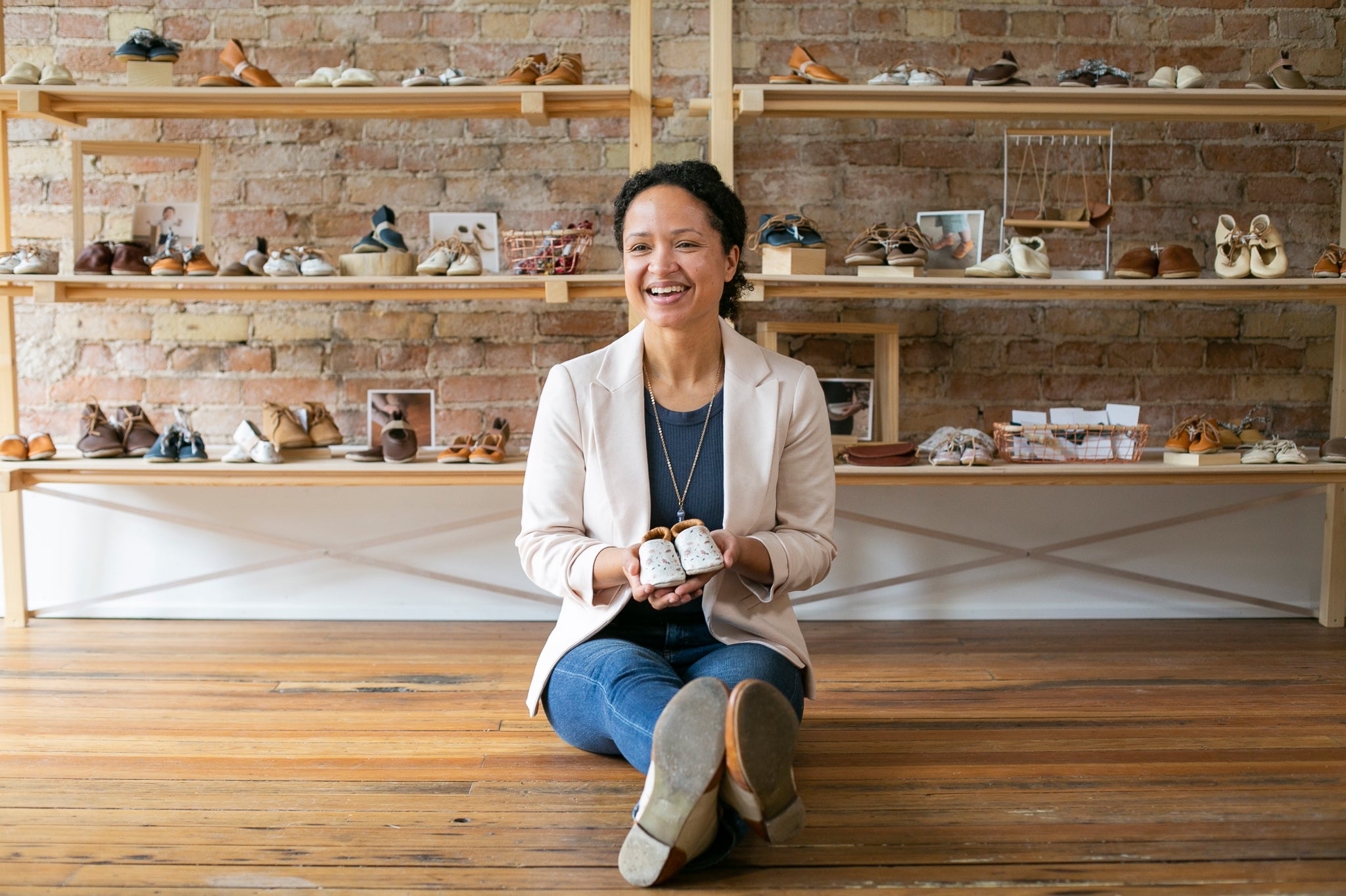 Founder of Sun & Lace sitting on floor of Stoughton Wisconsin storefront. She is holding a pair of handcrafted shoes and smiling.