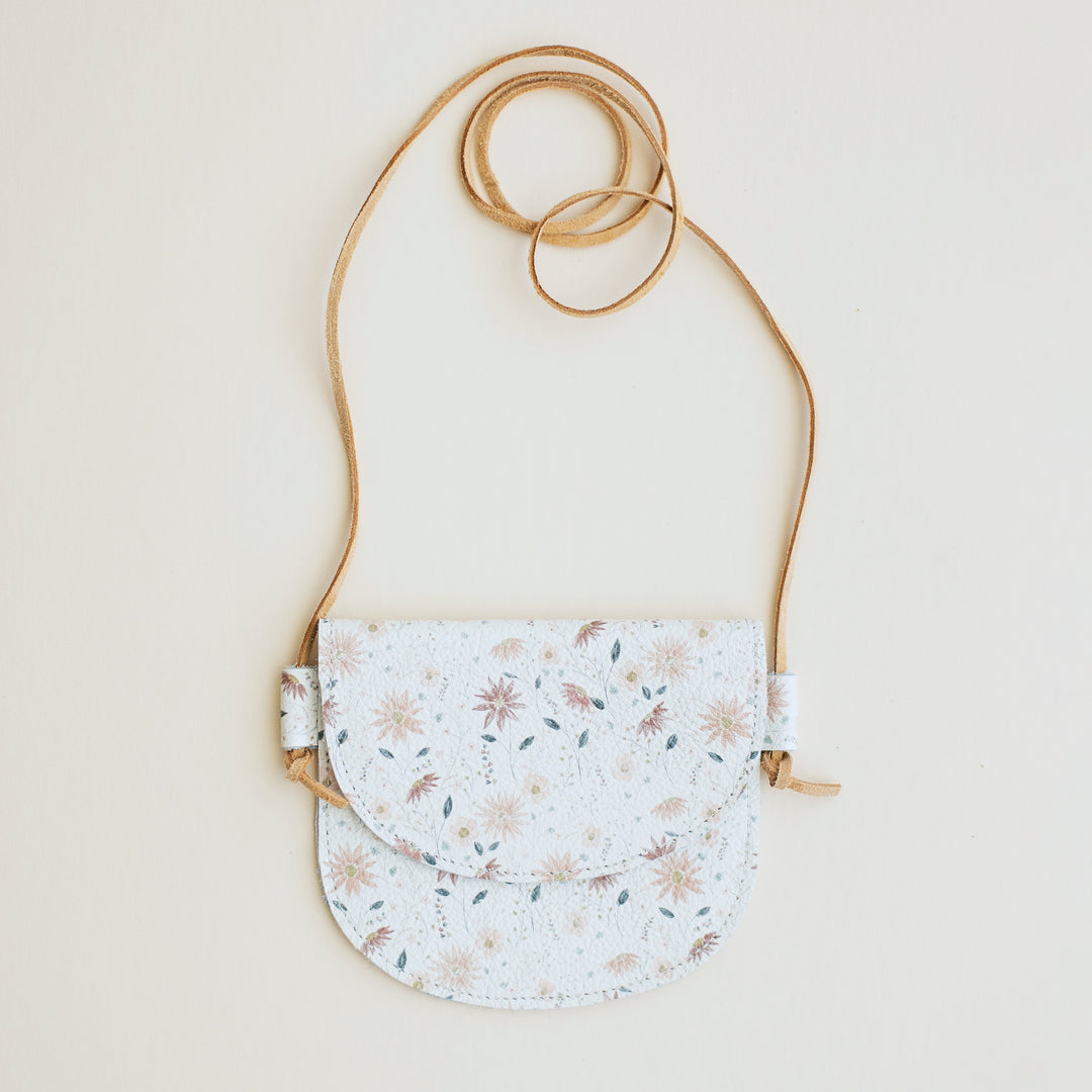 Small floral-patterned little girls purse with a strap on a light beige background