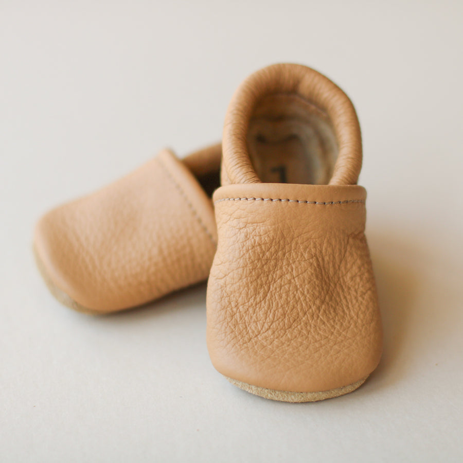 light brown leather gender neutral baby slip-on shoes. One agreed in front and top of other