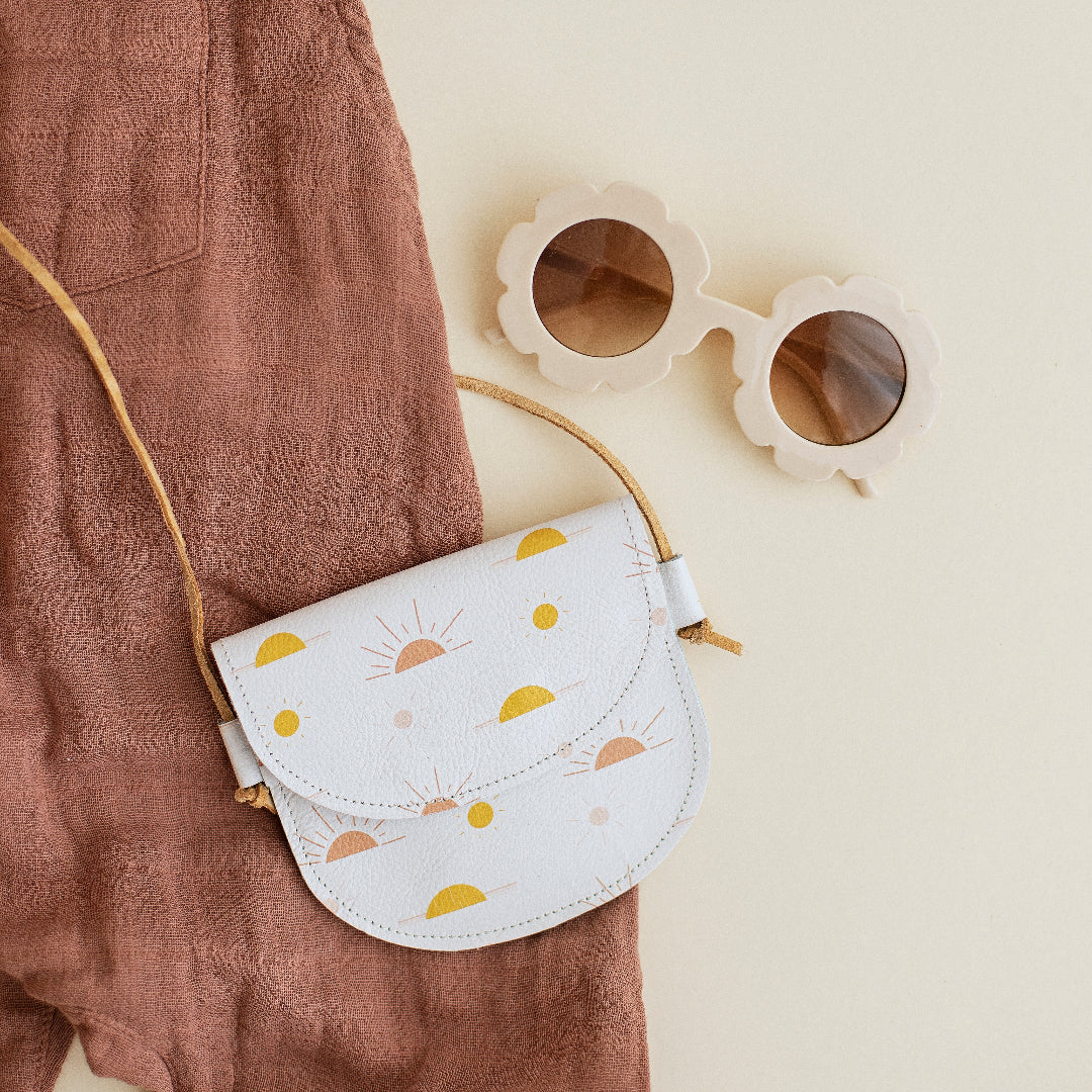 White crossbody bag with sun pattern and sunglasses on a beige background