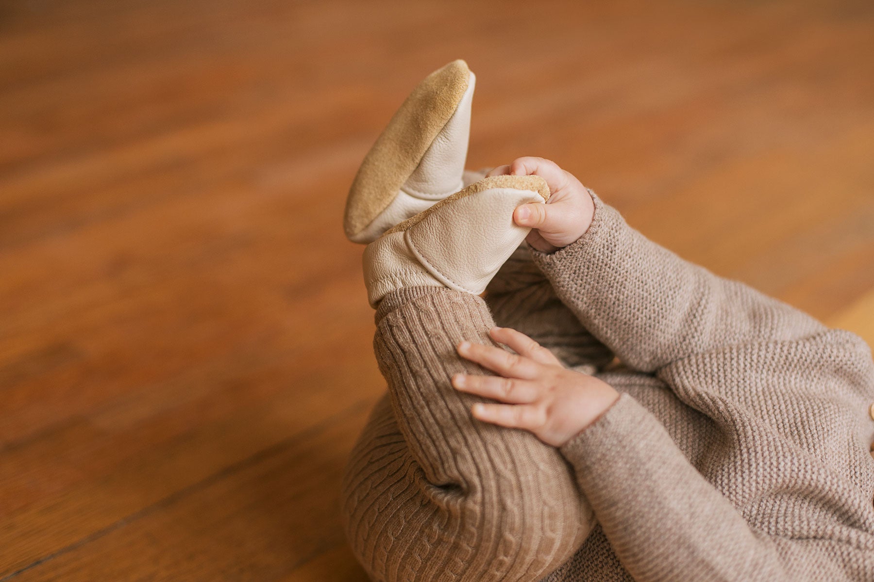 Baby lying on back with feet in the air. Wearing soft-soled cream baby shoes
