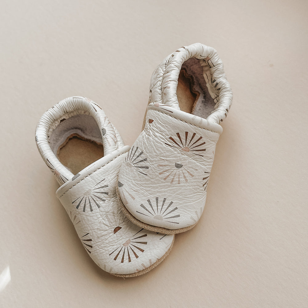 Pretty Please Teether's sunshine print on Sun & Lace slip-on shoes. Soft leather. Clay, sage, and beige sunshines on eggshell background