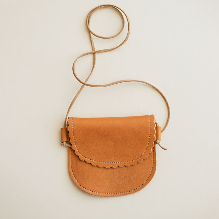 Product image of toddler leather purse in dark orange leather. Scalloped flap, toast suede lace strap. Cream background